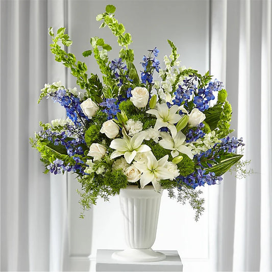 Express your condolences with the Sapphire Sympathy Pedestal Arrangement, a stunning floral tribute designed for funeral services, memorials, and sympathy gifts. This large, elegant arrangement is displayed in a classic pedestal vase, featuring a harmonious blend of white, blue, and green blooms, symbolizing peace, remembrance, and serenity.
Features:
Premium white lilies, snapdragons, and roses for purity and grace
Blue delphinium to add depth and tranquility